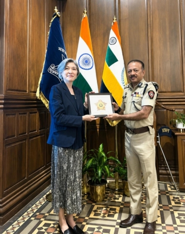 Deven Bharti presenting a Mumbai Police memento to a visiting official, with national and police flags behind.
